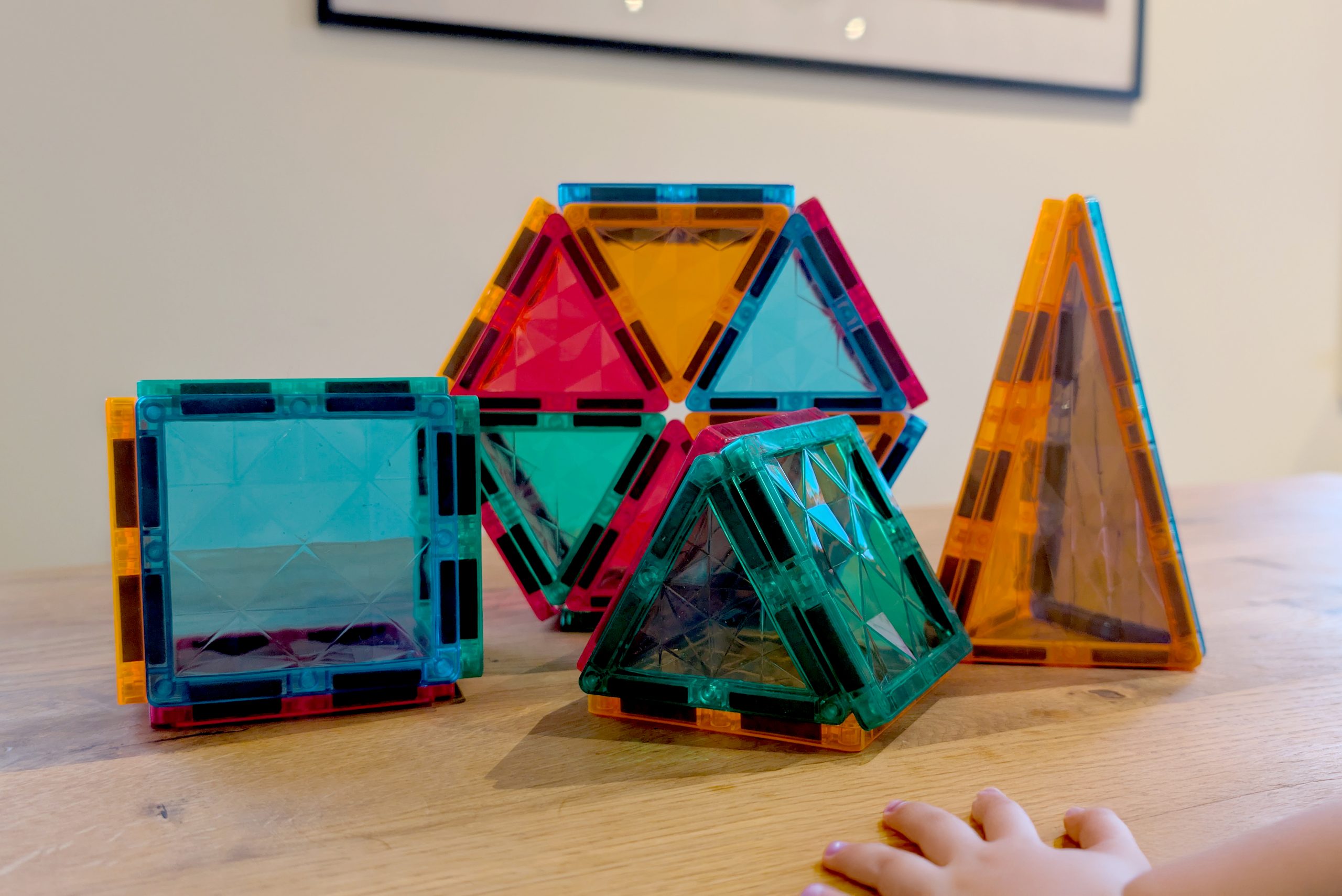 Färgglada Magna-Tiles i olika former, sammanfogade till ett torn, omgivna av byggdelar i klara färger. Perfekt för kreativ lek och lärande.